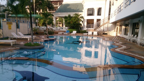 A swimming pool with dolphin designs, surrounded by lounge chairs and palm trees. - Camelot Hotel Pattaya (Pattaya)