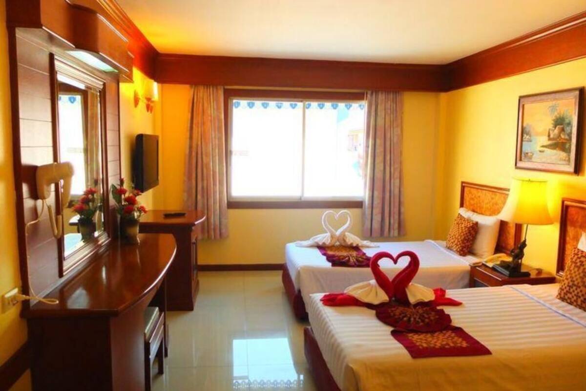 Una habitación de hotel con dos camas, un escritorio, un televisor y una ventana con cortinas.