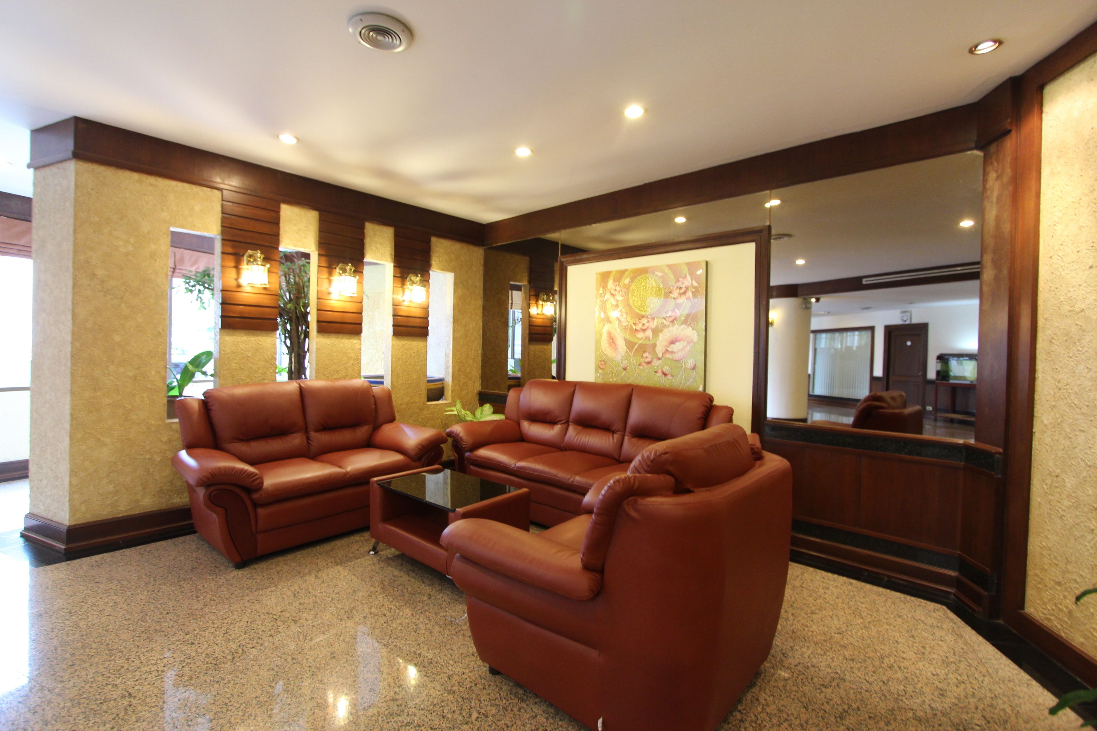 A lobby with brown leather sofas, a glass coffee table, and a large mirror reflecting the room.