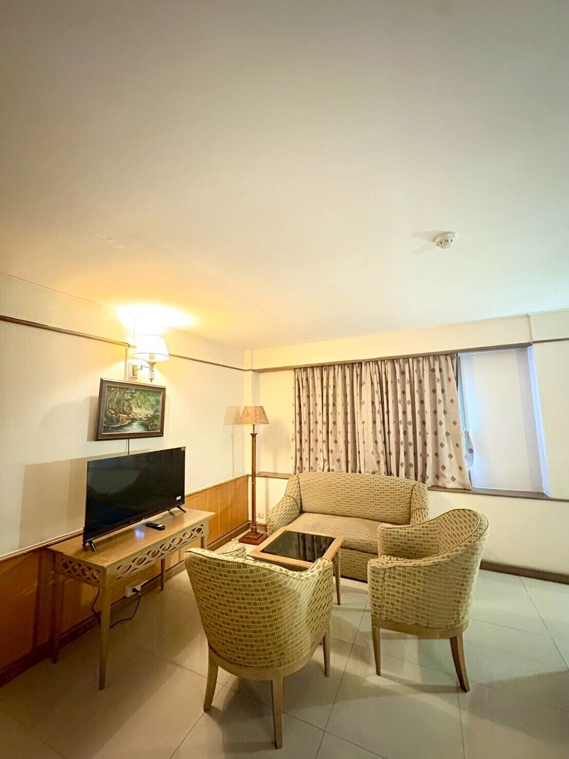 Ein Hotelzimmer mit Flachbildfernseher, einer Couch, zwei Korbstühlen, einem kleinen Tisch und einer Lampe.