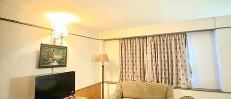 Ein Hotelzimmer mit Flachbildfernseher, einer Couch, zwei Korbstühlen, einem kleinen Tisch und einer Lampe.