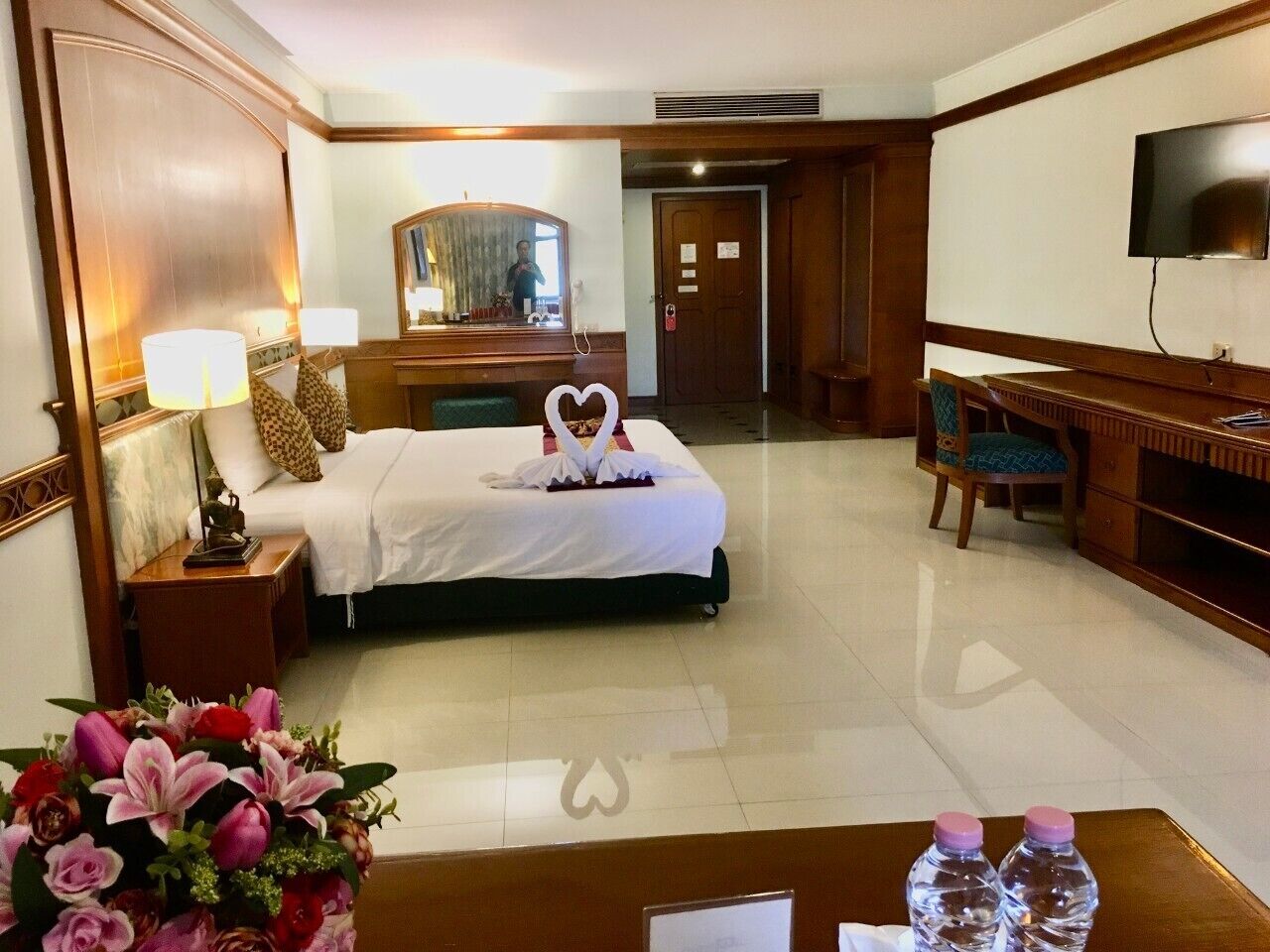 A hotel room with a bed, a desk, a chair, a TV, and a mirror.