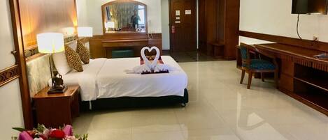 A hotel room with a bed, a desk, a chair, a TV, and a mirror.