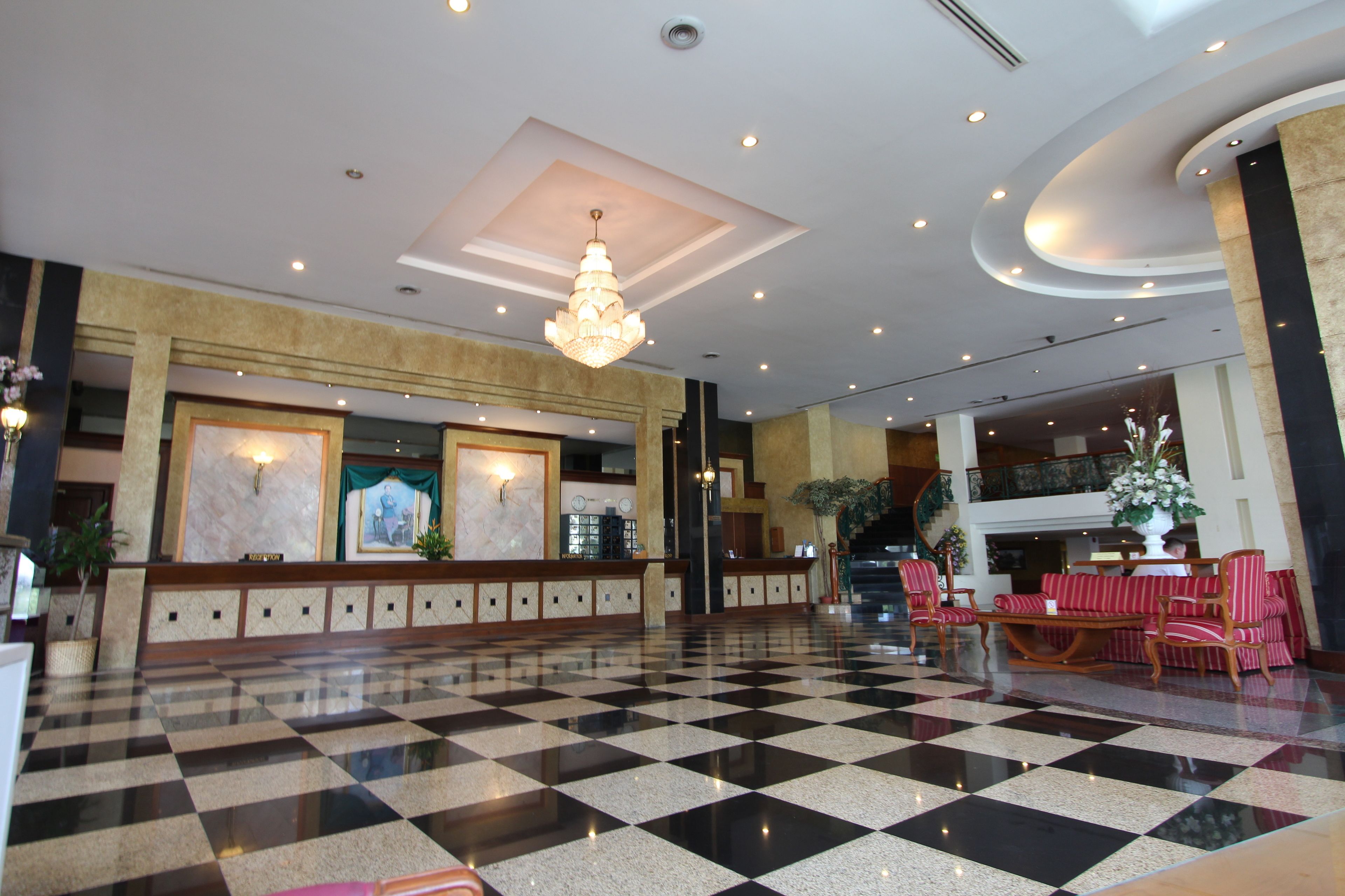 A lobby with a checkered floor, a chandelier, seating area, and a reception desk.