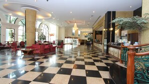 A hotel lobby with a checkered floor, red seating, and a staircase with ornate railings. - Camelot Hotel Pattaya (Pattaya)