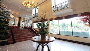 A spacious lobby with a grand staircase, a chandelier, and large windows offering a view of the outside. - Camelot Hotel Pattaya (Pattaya)
