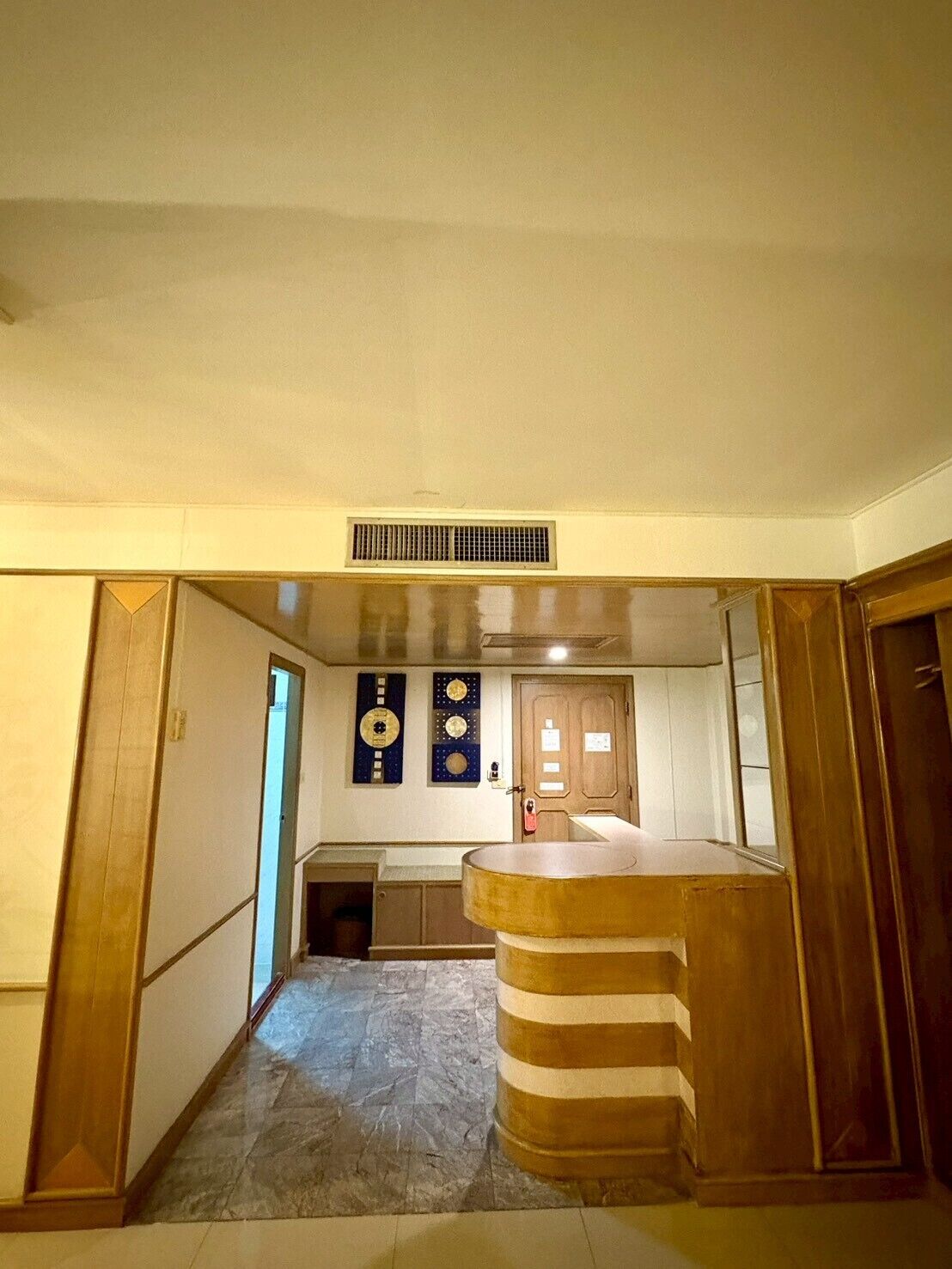 A hallway leading to a kitchen area with a central island, a vent on the ceiling, and a door at the end.
