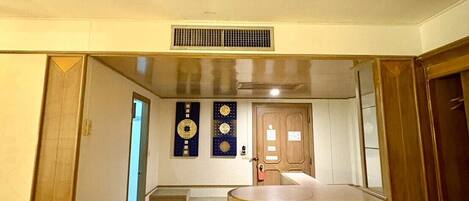 A hallway leading to a kitchen area with a central island, a vent on the ceiling, and a door at the end.