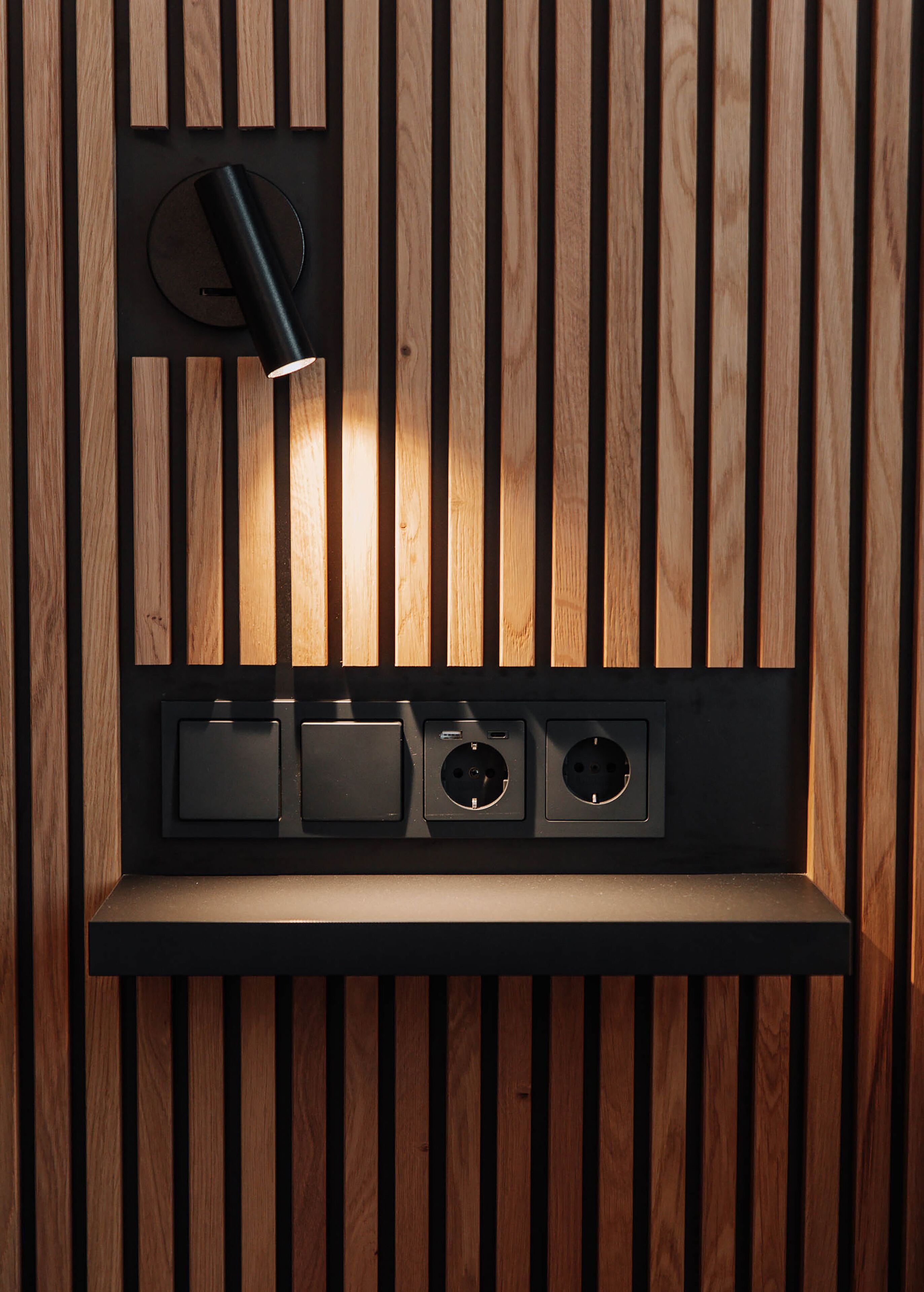 Una pared con listones de madera verticales y un estante empotrado con tres enchufes eléctricos.