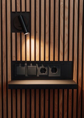A wall with vertical wooden slats and a recessed shelf with three black electrical outlets.