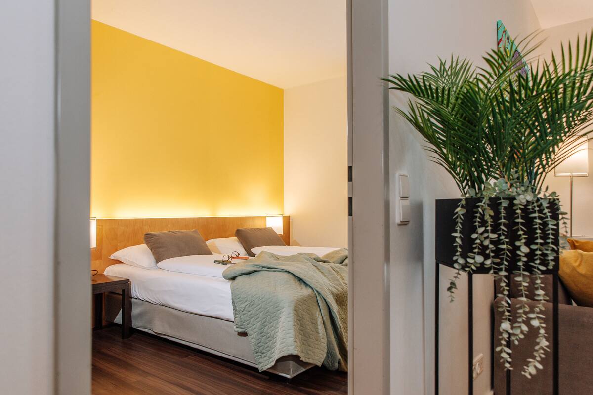 A hotel room with a bed, bedside table, and a large potted plant.
