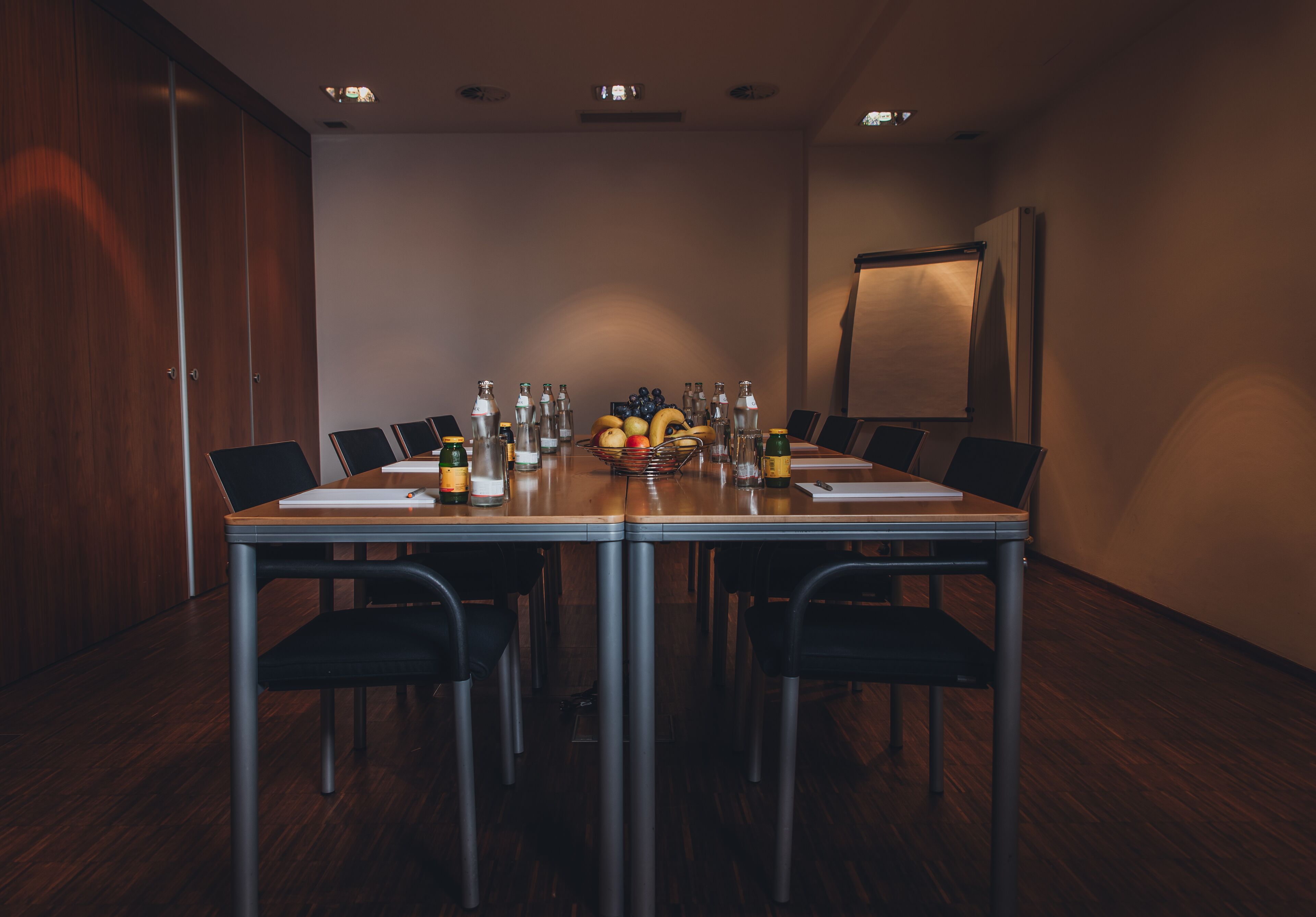 A conference room with a long table, chairs, a fruit basket, and various bottles.
