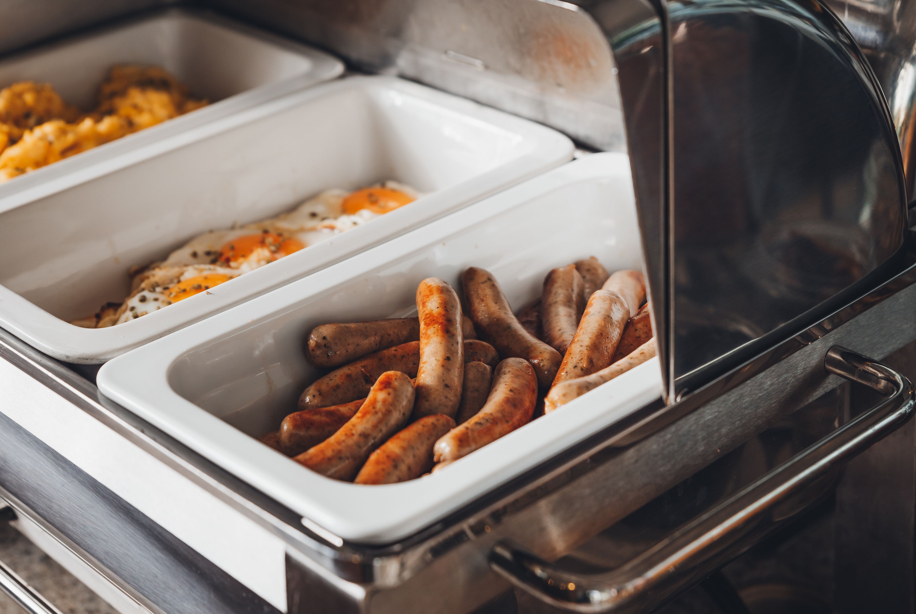 A buffet with two trays, one containing scrambled eggs and the other with sausages.