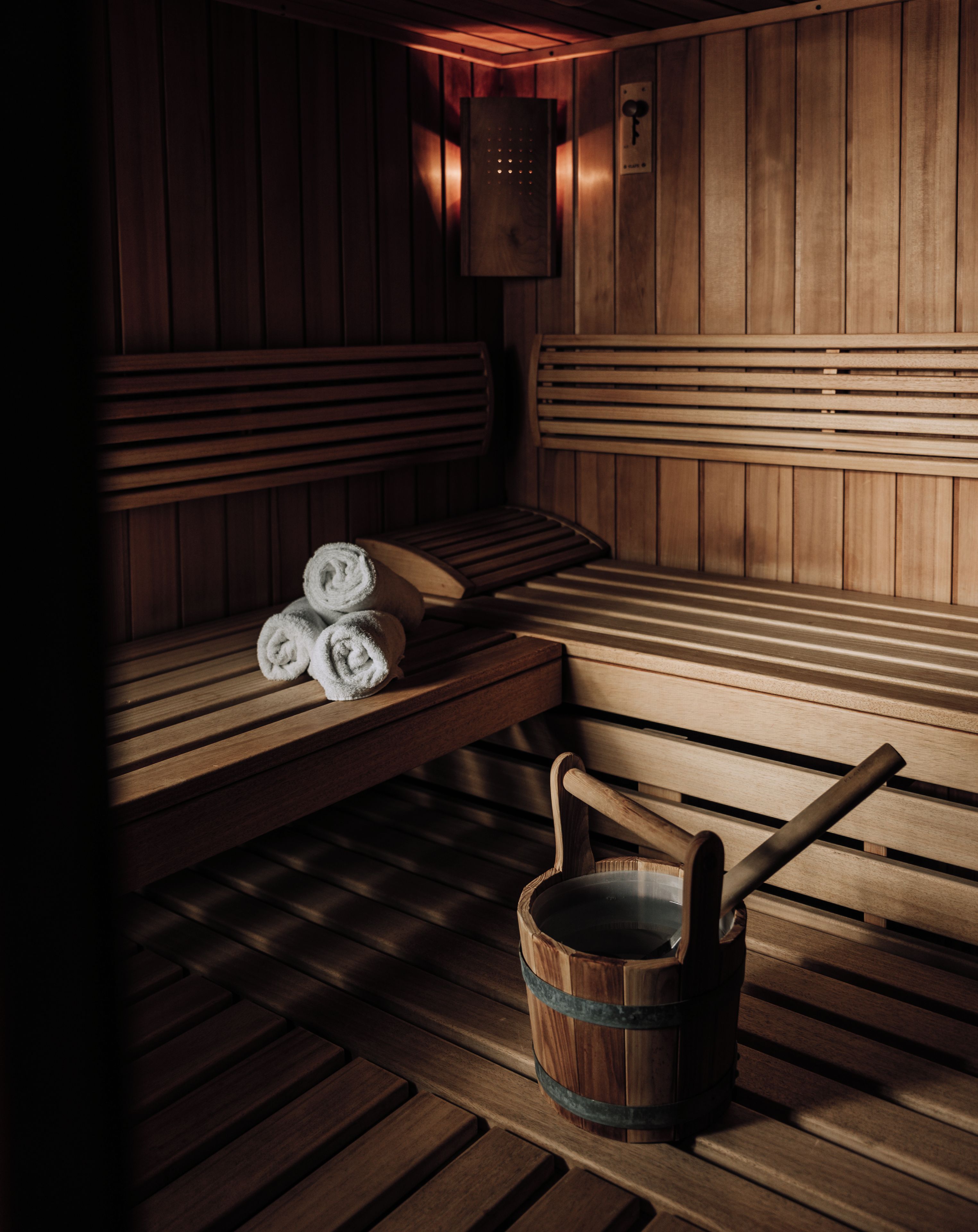 A sauna with wooden benches, a bench with towels, and a wooden bucket.