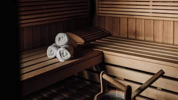 A sauna with wooden benches, a bench with towels, and a wooden bucket.