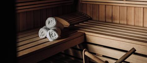 A sauna with wooden benches, a bench with towels, and a wooden bucket.