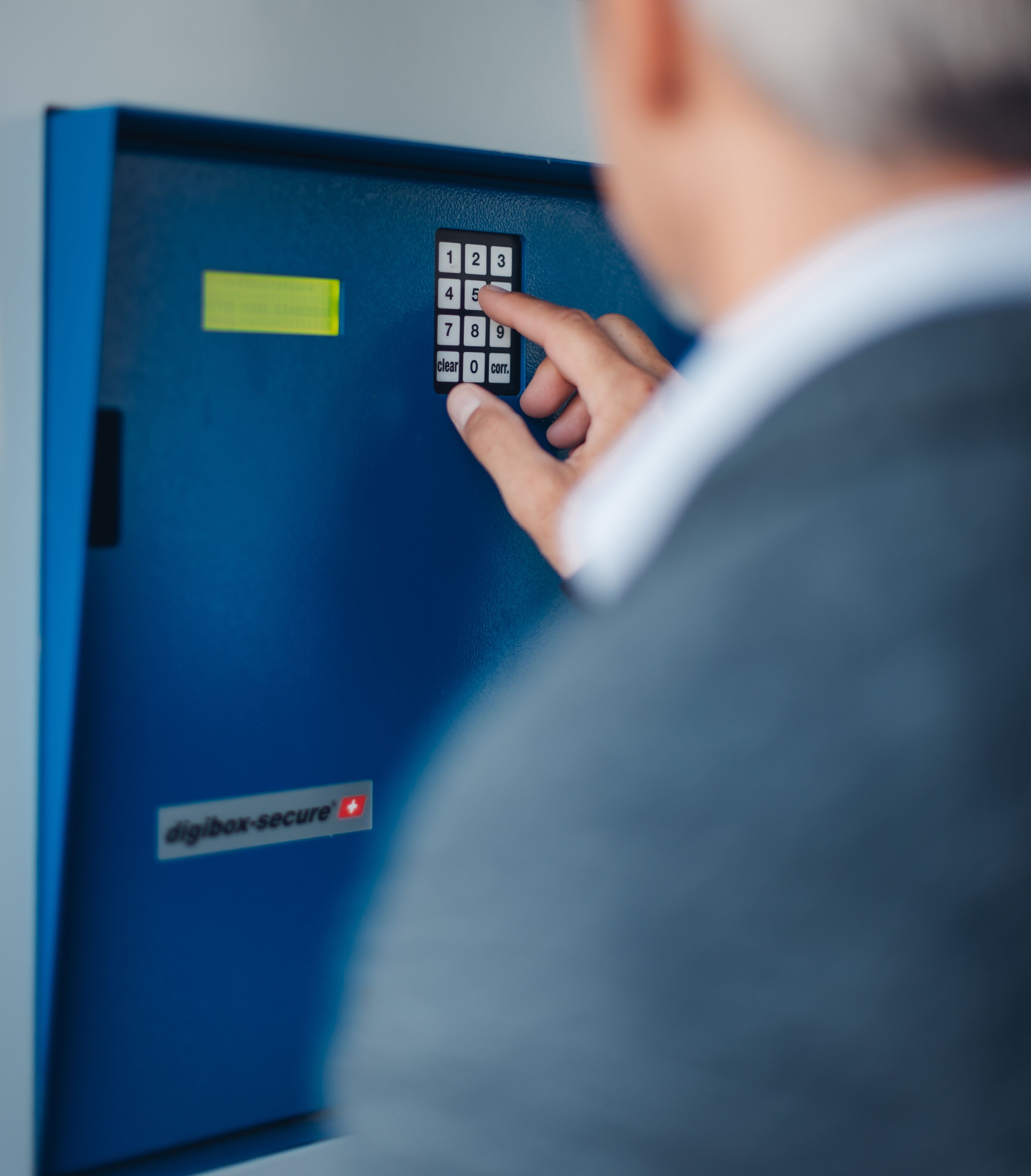En person benytter et blåt adgangspanel med et tastatur og en gul etiket.