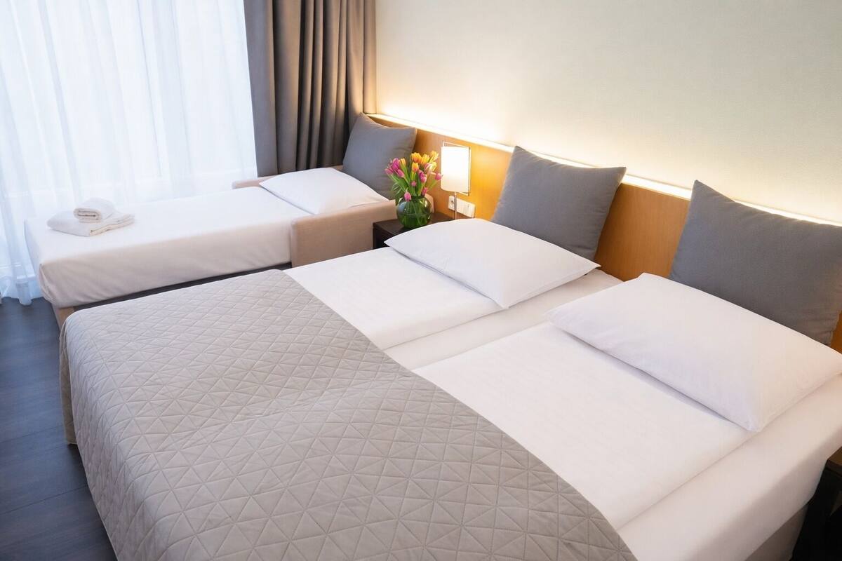 A hotel room with two single beds, a large bed, and a nightstand with a lamp and flowers.