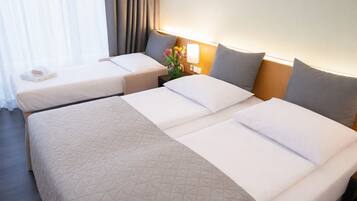 A hotel room with two single beds, a large bed, and a nightstand with a lamp and flowers.