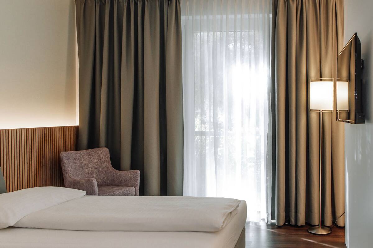 A hotel room with a bed, a chair, a TV, and curtains.