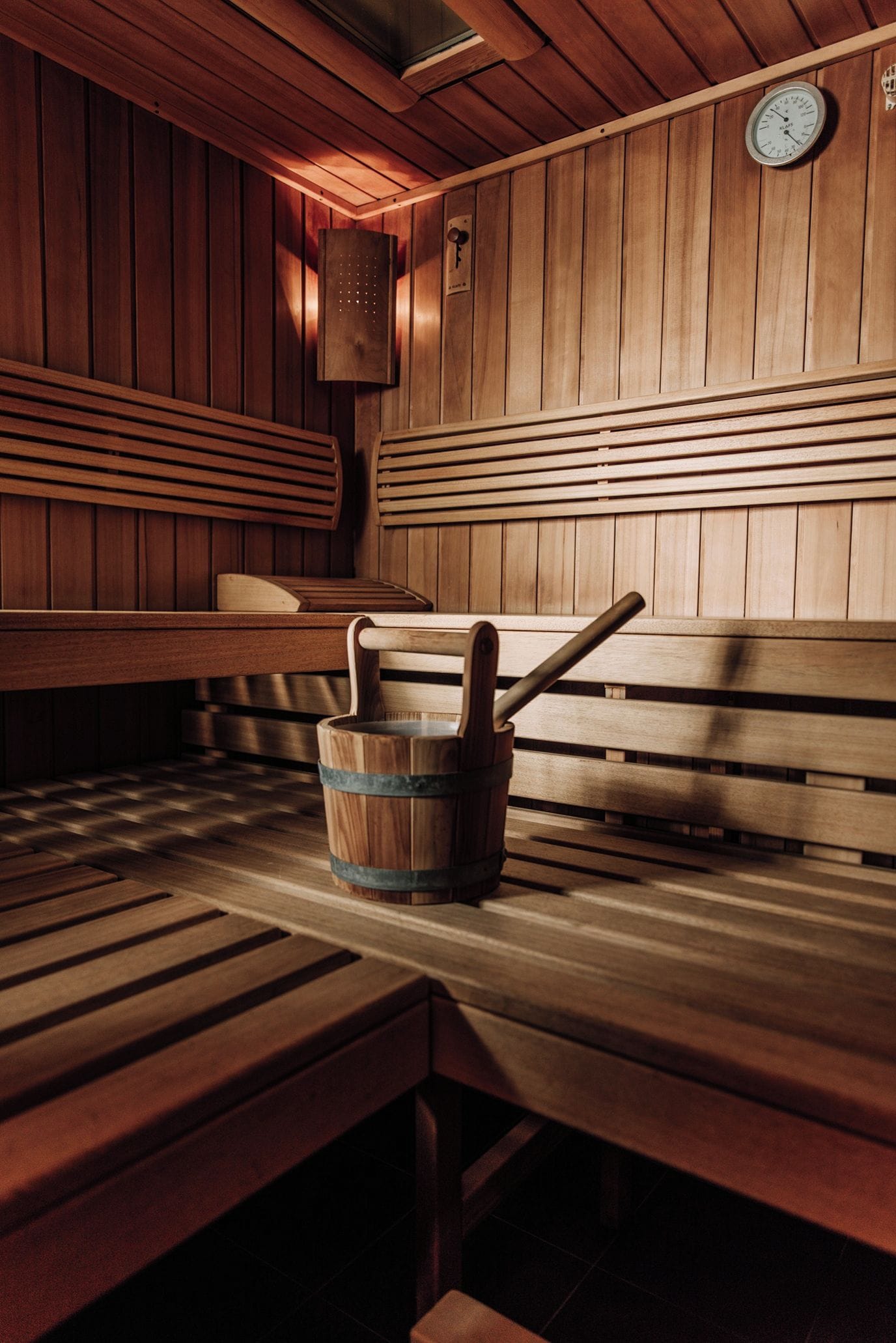 Una sala de sauna con bancos de madera, un balde de madera y un calentador fijado a la pared.