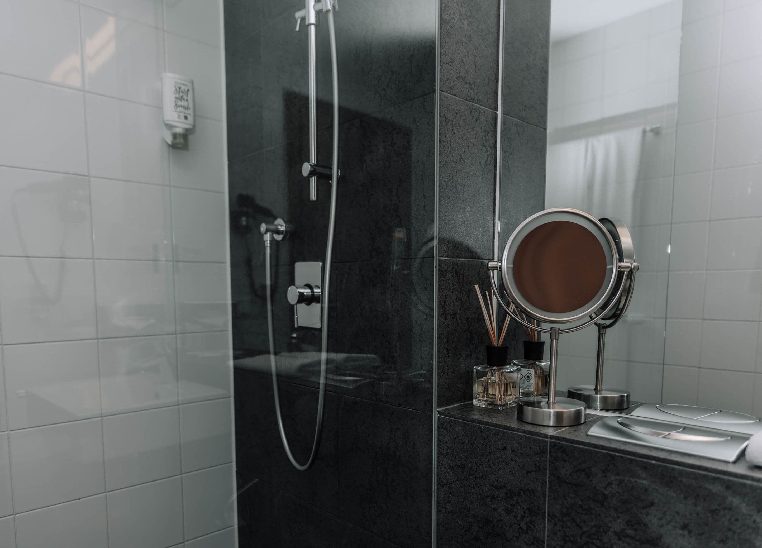 A modern bathroom with a glass-enclosed shower, a round mirror, and a small shelf with toiletries.