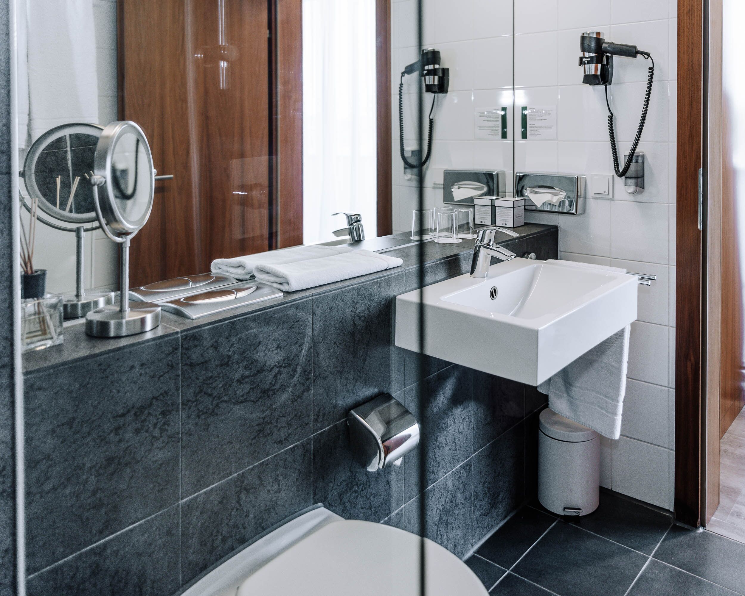 A modern bathroom with a marble sink, a mirror, a towel rack, a toilet, and a trash bin.