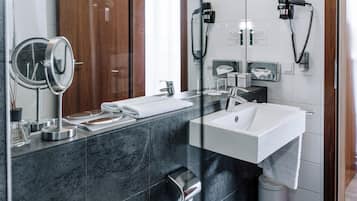 A modern bathroom with a marble sink, a mirror, a towel rack, a toilet, and a trash bin.