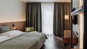 A hotel room with a large bed, a desk, a chair, a TV, and a window with curtains. - HEINhotel Vienna Airport (Schwechat)