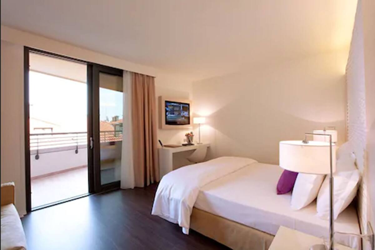 Una habitación de hotel con cama, escritorio, televisión y balcón.