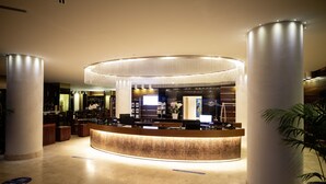A hotel reception area with a curved counter, large columns, and a modern chandelier. - Laguna Palace Hotel (Grado)