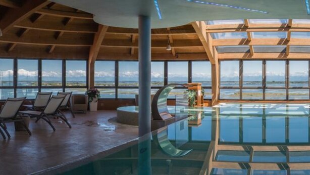 A spacious indoor pool with a view of the ocean, wooden ceiling beams, and seating areas. - Laguna Palace Hotel (Grado)