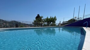 A clear blue swimming pool with a curved edge, surrounded by a concrete deck and metal fencing. - Residence Edy (Imperia)