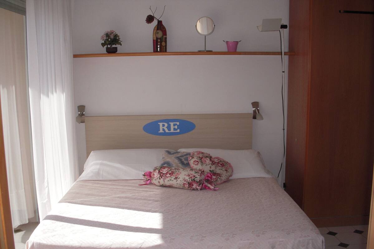 Una cama bien hecha con un cojín estampado con motivos florales y un cartel en la cabecera.