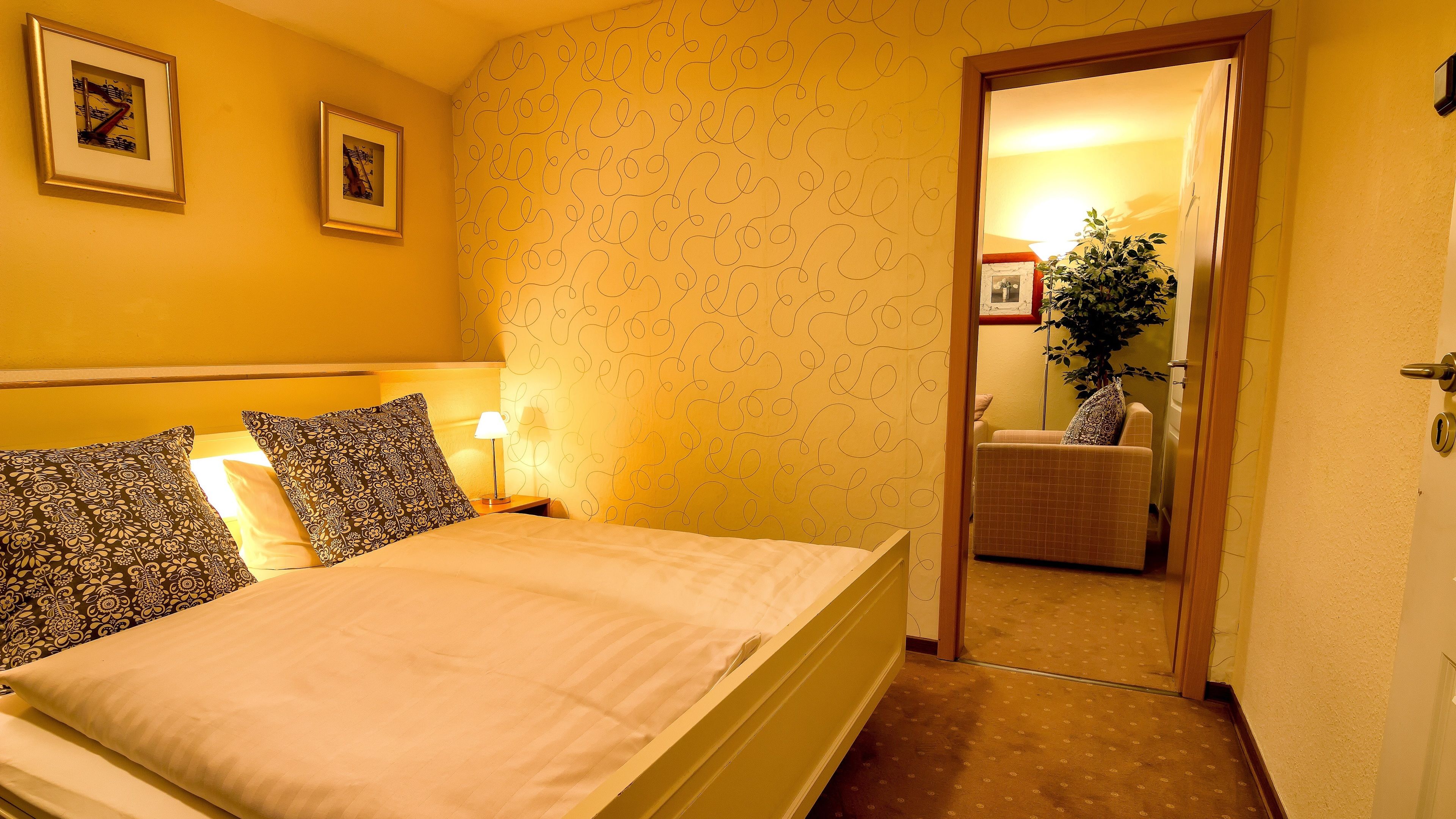 Una habitación de hotel con una cama, dos cuadros en la pared, una lámpara y una silla en la esquina.