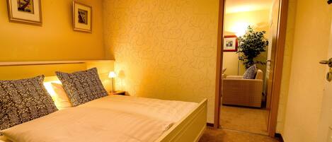 Una habitación de hotel con una cama, dos cuadros en la pared, una lámpara y una silla en la esquina.