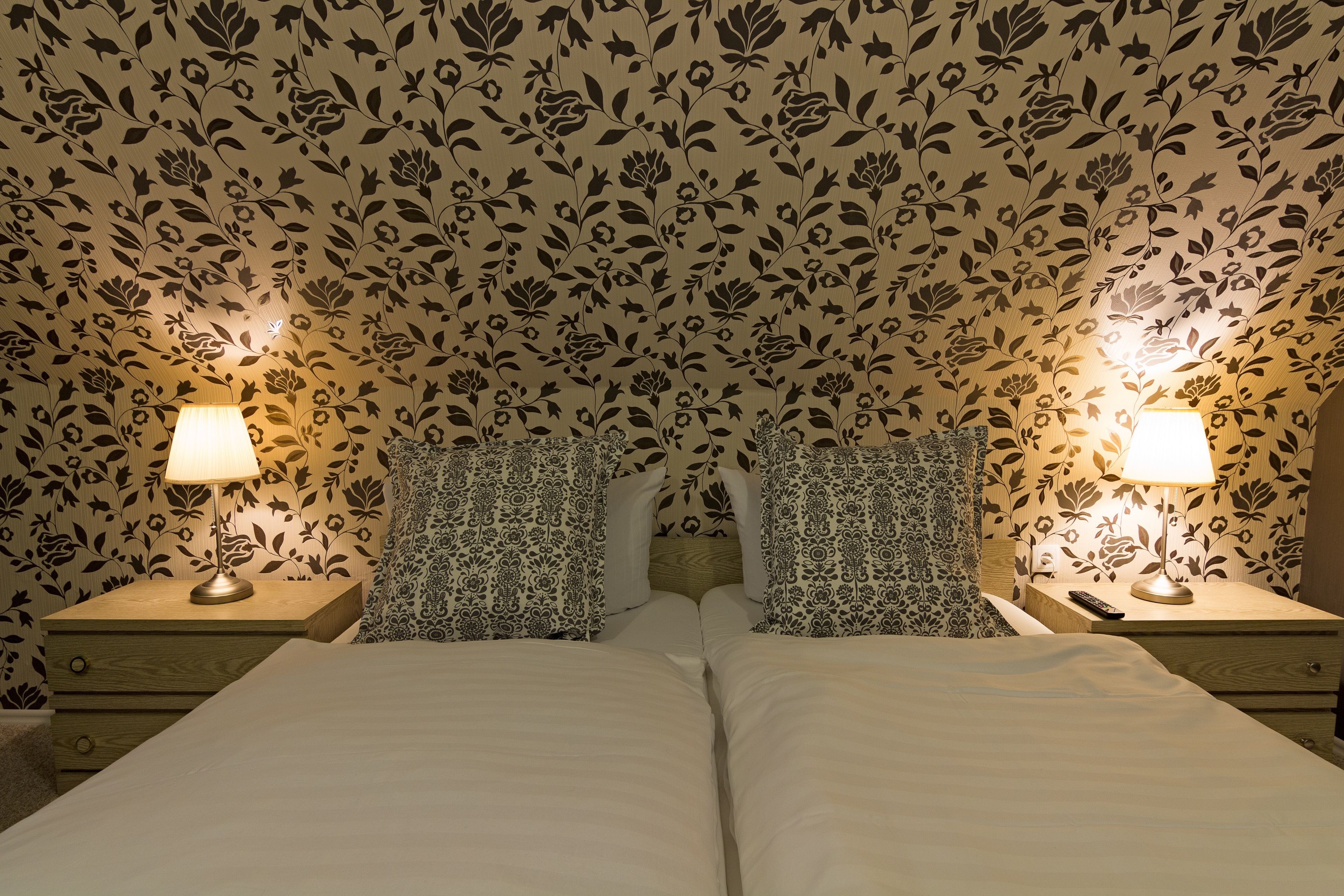 Ein Doppelbett mit zwei Nachttischen, an jedem Tisch eine Lampe und eine Fernbedienung. Der Raum hat Blumenpapier und gemustertes Bettzeug.