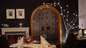 Un comedor con una mesa dispuesta para dos personas, una chimenea y una pared decorativa con motivos florales.