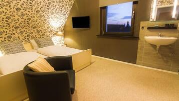 A bedroom with a bed, a chair, a TV, a window with a view, and a bathroom with a sink.