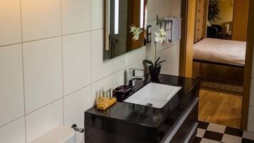 Un baño moderno con un lavamanos negro, azulejos blancos, un espejo y una pequeña planta en maceta.