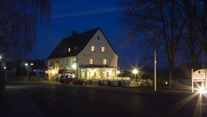 Un edificio de dos pisos con un letrero que indica que es un hotel. Hay coches estacionados adelante, y el edificio está iluminado por farolas.