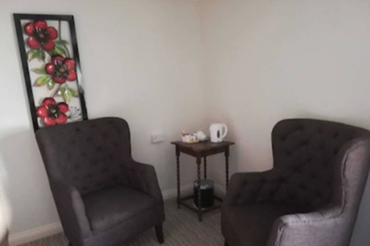 A room with two dark armchairs, a small table with a white mug, and a decorative wall piece.
