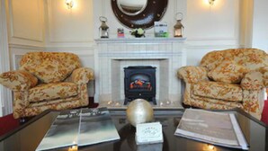 A room with two floral-patterned armchairs facing a fireplace with a decorative mirror above it. - Castle Lodge (Killarney)