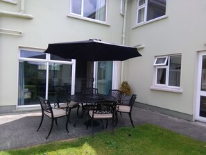 Un patio exterior con una mesa redonda y sillas, una sombrilla negra y una planta en maceta.