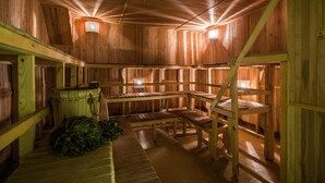 Un sauna en bois avec des bancs et une table en bois, un seau et quelques plantes vertes sur le sol.