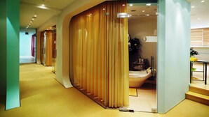 Un couloir d’hôtel moderne avec un mur incurvé et une baignoire visible à travers une cloison en verre.