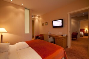 A hotel room with a bed, desk, chair, television, and a door leading to another room.