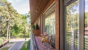 Un balcon avec des lattes en bois, une porte vitrée et des chaises en osier.