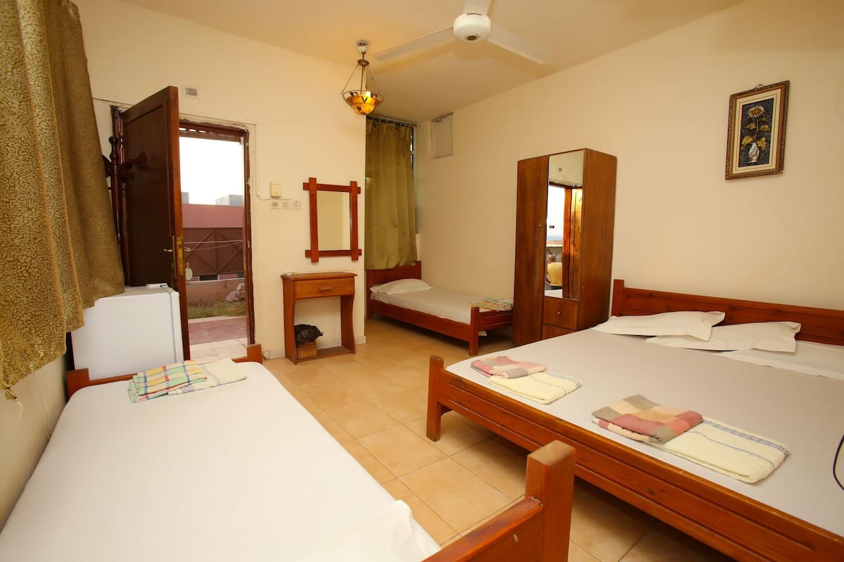 A room with three single beds, a wooden desk, a mirror, and a ceiling fan.