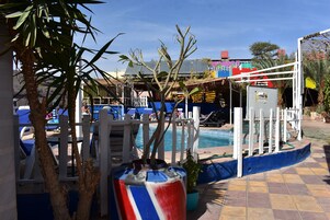 Zona de piscina con sillas de descanso, una cerca blanca y una maceta decorativa azul y roja.
